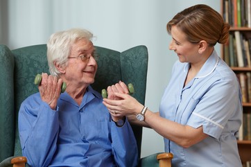 Carer assisting senior man with hand weights